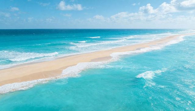 Aerial sandbar stretching diagonally through turquoise ocean with glimmering surf foam