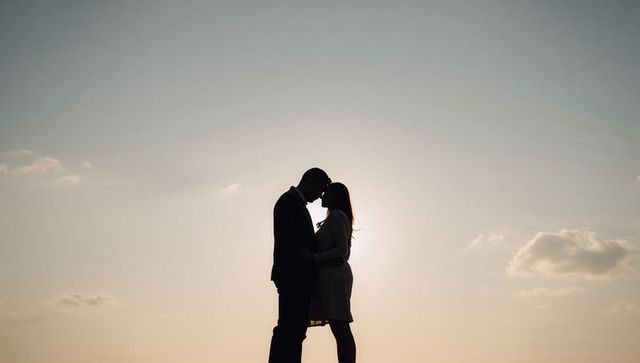Silhouette couple kissing at sunset on beach embracing under golden backlight