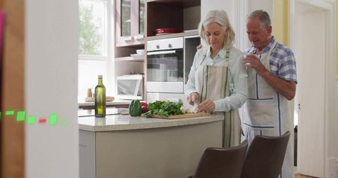 Mature couple preparing healthy meal in bright modern kitchen, woman chopping vegetables