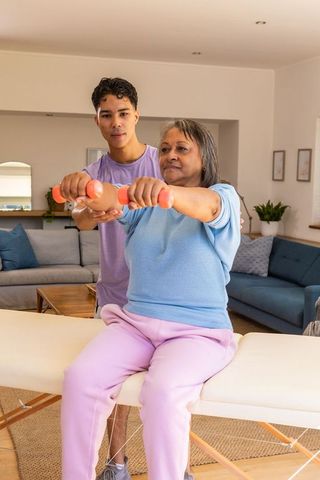 Senior woman exercising with trainer in living room during wellness session