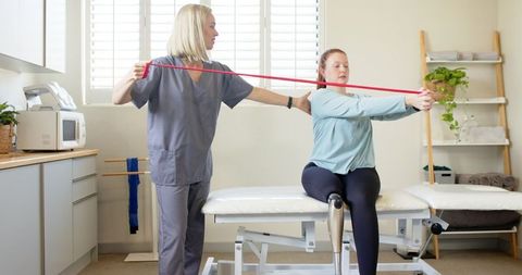 Therapist guiding prosthetic-leg patient in resistance band rehabilitation