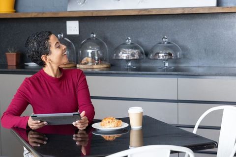 African american woman enjoying coffee and pastry while using tablet in modern cafe