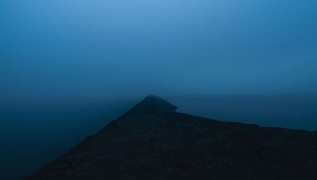 Narrow rocky jetty stretching toward foggy horizon over calm blue sea