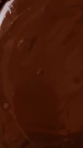 Vertical video glossy chocolate ganache flowing and smoothing in bowl, crumbs on rim