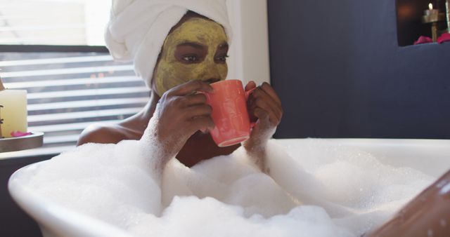 Woman relaxing in bath with bubbles, green face mask, and pink mug. Ideal for use in self-care, spa, wellness, beauty, or relaxation themes. Highlights the importance of taking time for personal wellness and pampering. Suitable for articles and advertisements focused on home spa treatments or relaxation tips.