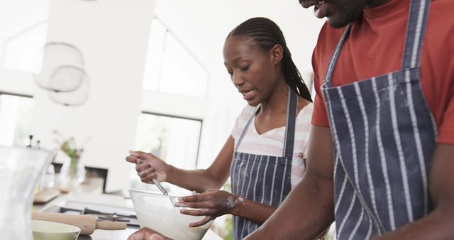 Engaging scene of couple wearing aprons baking together in a bright and modern kitchen. Useful for promoting family activities, culinary classes, relationship bonding, and home lifestyle.