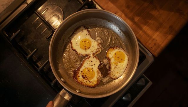 Stainless skillet cooking sunny-side-up eggs with cracked pepper on gas stove