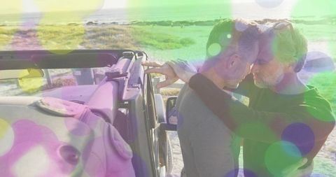Middle-aged men sharing intimate forehead touch by coastal jeep with dreamy bokeh