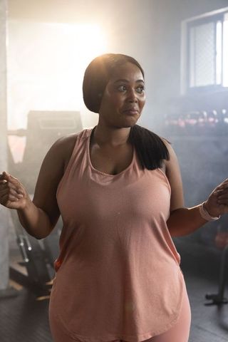 African american woman jumping rope in gym wearing pink activewear with backlight glow