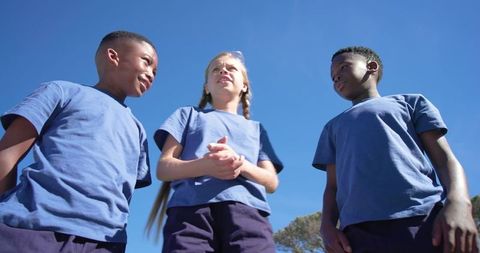 Diverse elementary schoolchildren standing together in blue uniform shirts under bright blue sky