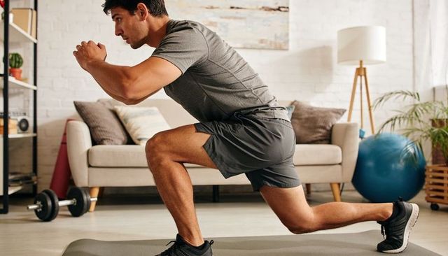 Man performing forward lunge on mat in living room for home workout and strength training