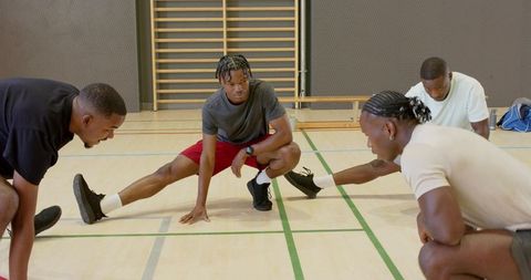 African american men performing side lunges in indoor gym preparing for team training