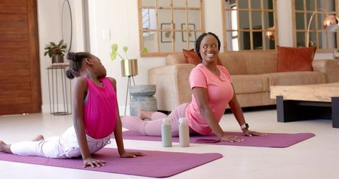 African mother and daughter practicing yoga at home on purple mats smiling and stretching