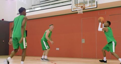 Multiracial basketball players practicing layup and passing, celebrating teamwork on court