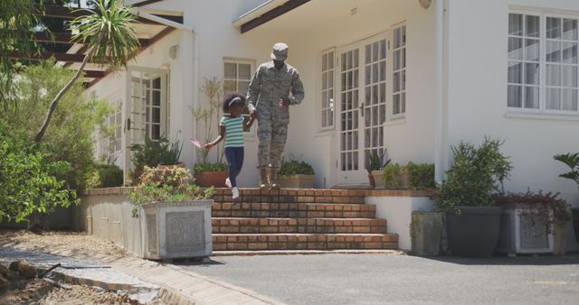 Happy african american male soldier and his daughter holding hands outside the house. Military, patriotism, family, and togetherness.