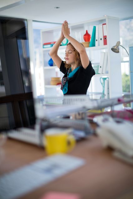 This photo shows a female executive practicing yoga at her desk in an office environment, embracing mindfulness and stress relief. It can be used in articles and advertisements promoting workplace wellness, office fitness programs, and the importance of taking breaks for mental health. Perfect for illustrating themes of balance and corporate well-being.