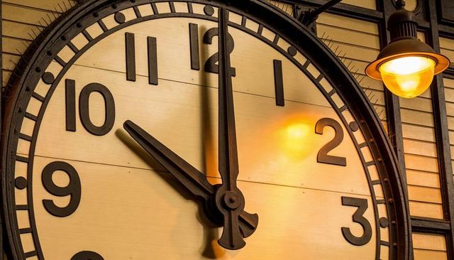 Retro industrial round wall clock closeup with bold numerals and warm amber lamp glow
