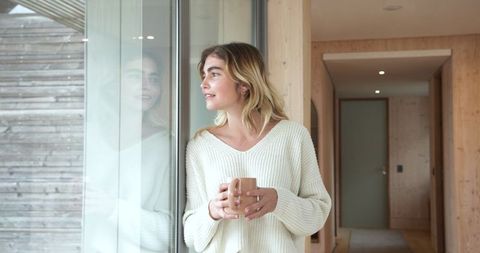 Cozy Tranquility: Woman Gazing Through Glass Door Holding Mug