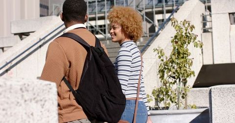 Diverse college students walking and talking on sunlit urban campus terrace with backpacks