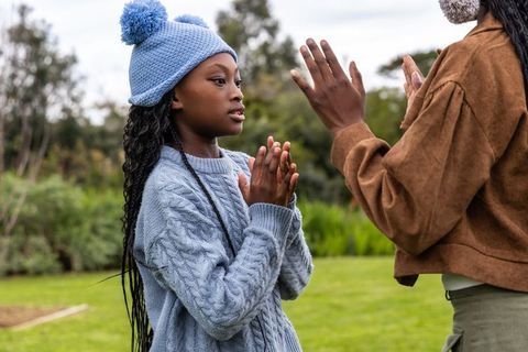African-american daughter and parent clapping outdoors in knit sweater and pom beanie