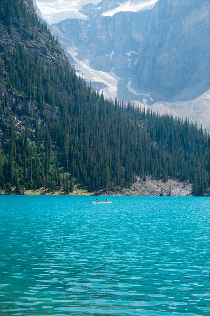 This image shows people kayaking on a turquoise lake surrounded by tall evergreen trees and mountains in the background. Ideal for use in travel brochures, adventure sports promotions, or outdoor activity websites.