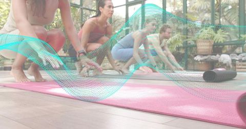 Women Practicing Yoga Stretching on Pink Mats in Glass Greenhouse Studio for Group Wellness