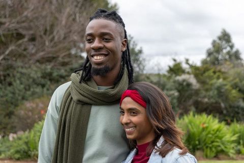 Smiling african american man and indian woman standing relaxed in park on overcast day