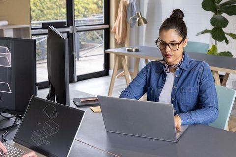 Woman working on laptop in modern coworking studio with multiple monitors and wireframes