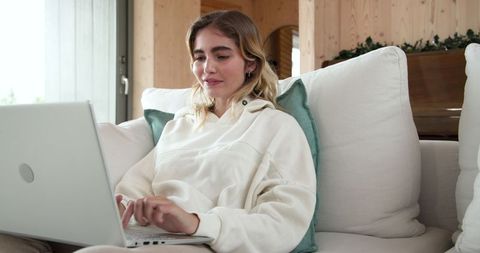 Young woman relaxing with laptop on cozy sofa in modern living room