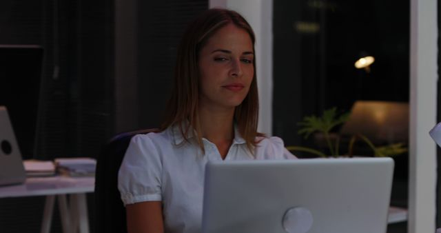 Businesswoman working late at office desk with laptop. Perfect for illustrating concepts of hard work, dedication, overtime, office life, late-night assignments, and focus. Useful for articles or advertisements about work-life balance, productivity tips, or corporate culture.