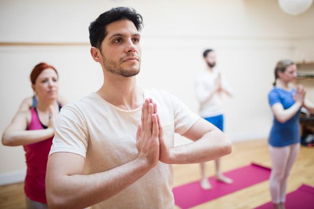 Group of people practicing tree pose during yoga class in fitness studio. Ideal for content related to fitness, wellness, group activities, indoor workouts, and promoting a balanced lifestyle.