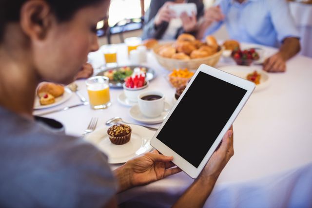 Businesswoman using digital tablet during breakfast meeting in restaurant. Ideal for illustrating modern business practices, technology in professional settings, and networking over meals. Suitable for articles on business communication, remote work, and professional lifestyle.