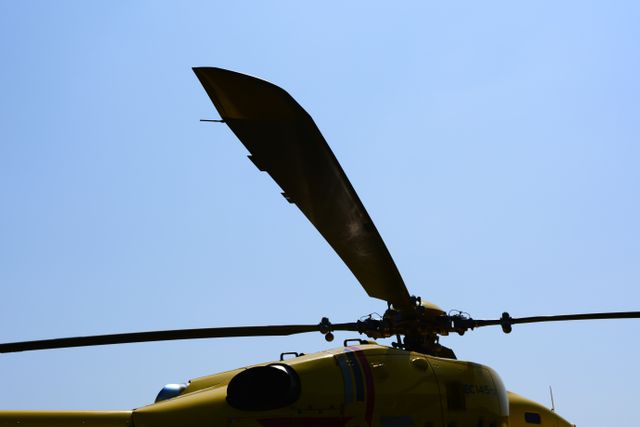 Silhouette of a helicopter rotor blade against a clear blue sky, capturing the essence of aviation technology and emergency services. Could be used for topics related to aviation, rotorcraft mechanics, air rescue missions, and transportation technology. Ideal for educational materials, aviation-related content, and emergency response promotions.