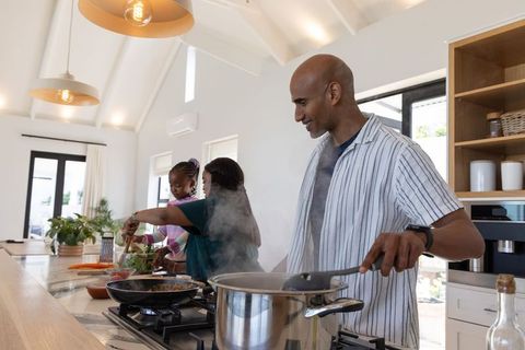 Indian father and family cooking together in bright modern vaulted kitchen