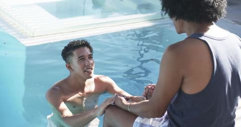 Two men holding hands and smiling at backyard pool enjoying sunny outdoor moment
