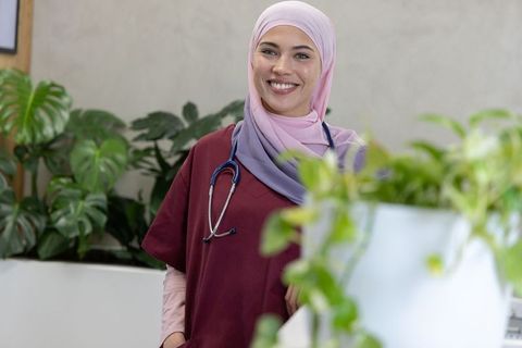 Smiling african american nurse wearing hijab and scrubs with stethoscope at reception desk