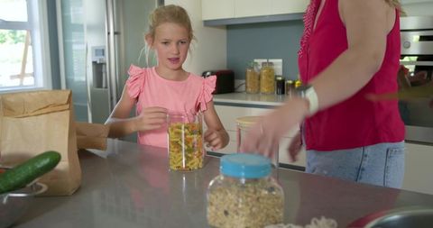 Mother and daughter unpacking groceries in bright modern kitchen organizing pasta jar