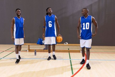 African american basketball team standing on indoor court holding ball during practice