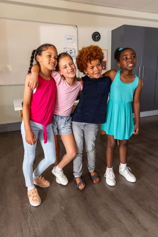 Diverse elementary friends embracing and smiling in classroom celebrating friendship