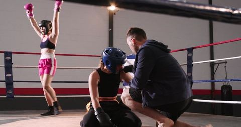 Trainer Tending Kneeling Boxer While Opponent Celebrating Victory in Gym Ring