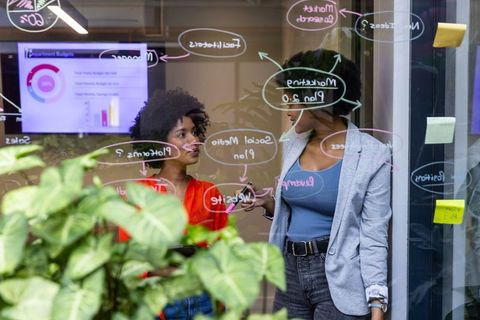 African American Businesswomen Collaborating with Glass Board