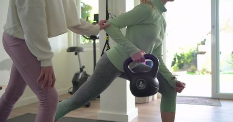 Female personal trainer coaching reverse lunge holding 8kg kettlebell during home workout