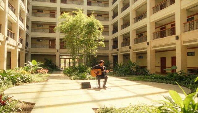 Solo musician performing acoustic guitar in sunlit hotel atrium with amp and microphone
