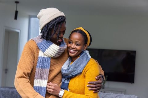 African american couple embracing in cozy home wearing scarves and knitwear