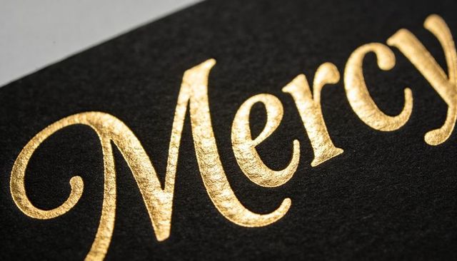 Shining gold foil mercy lettering on black card, macro luxury detail