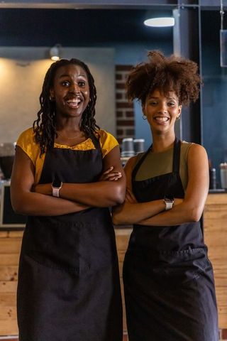 African american baristas standing proud behind cafe counter smiling in black aprons