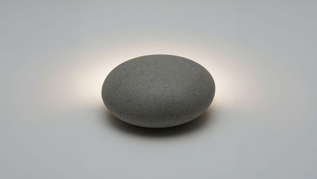 Pebble lamp emitting warm halo on minimal concrete tabletop, sculptural backlit design