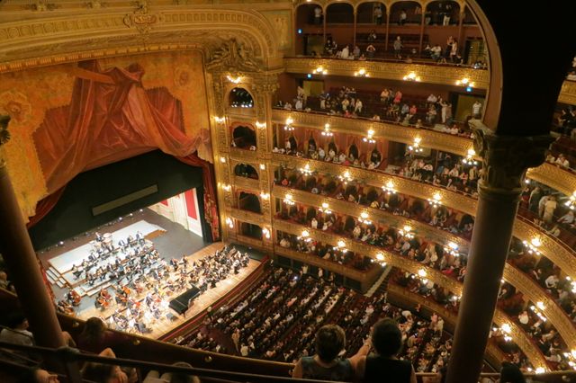 Orchestra performing live at historic opera house viewed from balcony. Audience enjoying elegant classical music experience in a grand architectural setting. Suitable for content related to culture, arts, music events, and architectural heritage.