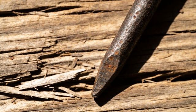 Rusted chisel tip resting on splintered wood plank close-up showing corrosion and texture