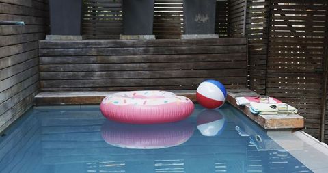 Pink donut pool float floating in courtyard plunge pool with beach ball and sunglasses